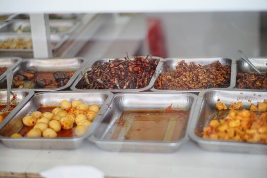 Various kinds of traditional Indonesian side dishes served in stainless steel trays at a local food stall.