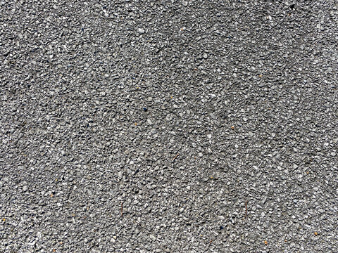 A rough gray asphalt surface with small rocks and gravel creates a solid durable and textured ground often used for roads driveways or outdoor paved areas