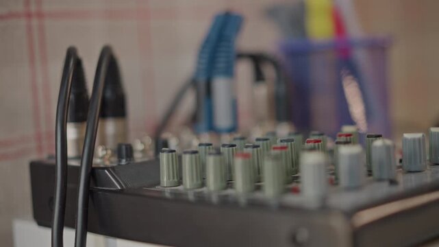 Mixing console with connected cables and jacks student musician patches channels while instructor prepares levels for school rehearsal, neutral plaid background and shallow focus emphasize gear