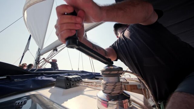 Close-up of a man operating a winch and handling ropes on a sailing yacht. Nautical equipment, sailing lifestyle, yacht operation, sea travel and summer boating adventure.