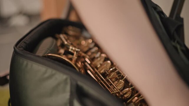 Caucasian band coach checking saxophone keys inside bag careful touch across brass keys subtle adjustments to alignment intimate rehearsal space soft carpet under chair hands demonstrating maintenance