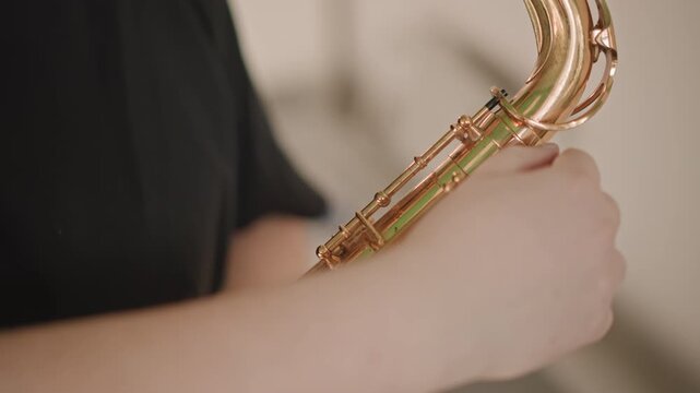Closeup saxophone body and keys in warm studio soloist prepares instrument with careful grip, subtle shine on brass, practice posture and breath control visible, ambient lighting highlights keywork