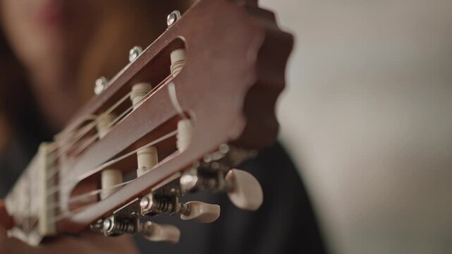 Instructor provides detailed tuning demonstration on guitar in friendly setting. Instructor expertly guides students through proper guitar peg adjustment with supportive mentorship
