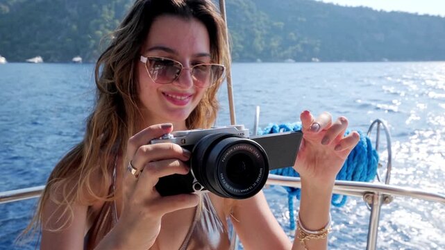 Young woman filming with a digital camera on a yacht at sea. Summer vacation, travel content, boating lifestyle, blue water, photography and relaxed nautical leisure.