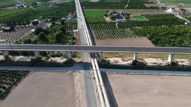 Aerial drone view of a modern high speed train railway bridge crossing the Tajo Segura water transfer pipeline surrounded by agricultural orchards at the Huerta de Orihuela in Spain
