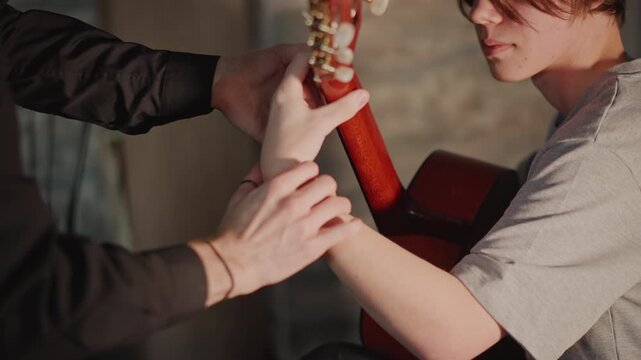 Instructor assists student. Mentor helps tune guitar. Educational session with careful instrument adjustment. Teacher patiently guides student through guitar tuning process in studio
