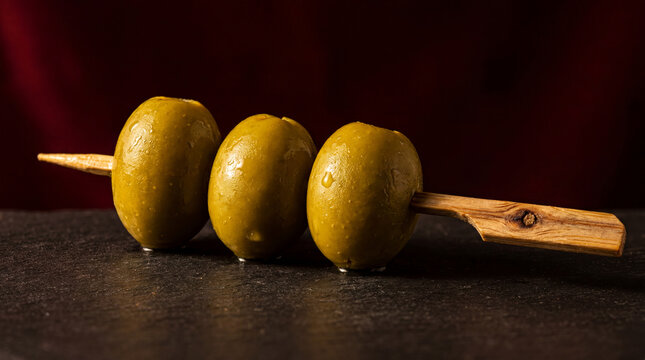 Green olives on wooden skewer on black slate board, gourmet food ingredient and appetizer concept.