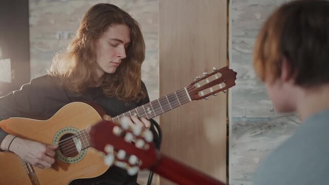 Young caucasian guitar coach teaching student, intimate studio lesson with acoustic guitar, warm backlight, focused chord demonstration, attentive pupil taking notes, supportive mentorship vibe
