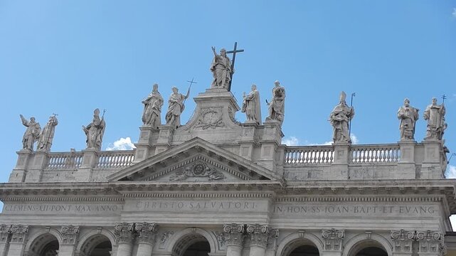 Lord Jesus Christ and saints - statues at top of facade of Basilica of St. John in Lateran in Rome i Italy and blue sky with slowly moving white clouds. Topics: church, Christianity, faith, history