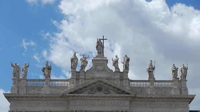 Lord Jesus Christ and saints - statues at top of facade of Basilica of St. John in Lateran in Rome i Italy and blue with slowly moving white clouds. Topics: church, Christianity, faith, history