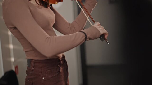 Female artist finetuning her violin. She adjusts her violin with precision during warmup session. Female musician finetunes her violin and bow storing concentration before rehearsal