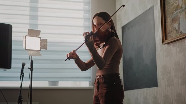 White woman recording violin in studio, standing beside microphone and softbox light, student tracking melody for school project, focused posture and expressive playing, modern classroom meets