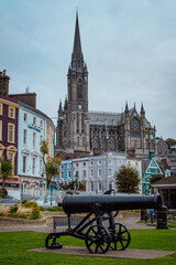 Naklejka premium Historic cannon with colorful town houses and St Colman's Cathedral in Cobh, Ireland