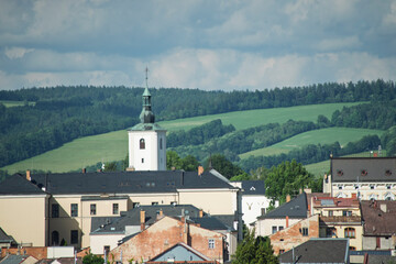 Obraz premium A beautiful panoramic view of a charming small European town nestled among lush green hills, agricultural fields, and forests under a cloudy blue sky. The cityscape features traditional architecture w