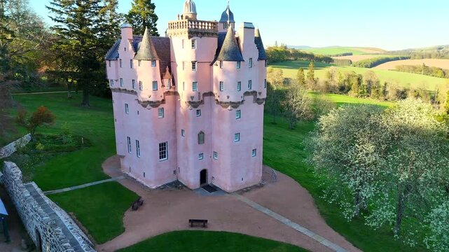 Craigievar Castle is shown in a cinematic video with a smooth circling camera orbiting around the castle, revealing its pink towers, surrounding forest, and rolling Scottish hills from every angle.