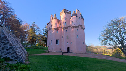 Craigievar Castle appears in a close daytime view, its pink stone glowing under bright sunlight, with clear skies revealing every detailed tower and carved architectural feature. © Ashgan