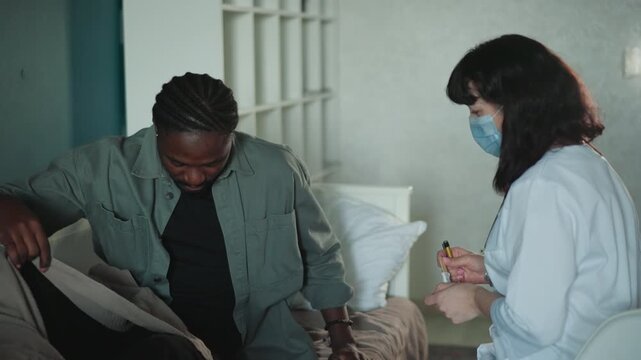 Nurse offers medication to sitting patient at bedside in bedroom, gentle counseling and handson guidance, mask and white coat create protective clinical tone with supportive homecare environment