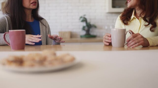 Women in their 40s discussing recent news while drinking tea at home