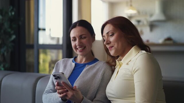 Cheerful women friends in their 40s browsing dating app on smartphone for fun
