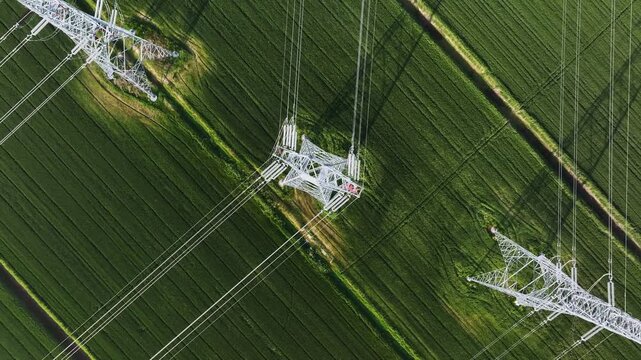 Aerial view of high voltage transmission towers and cables over green agricultural fields