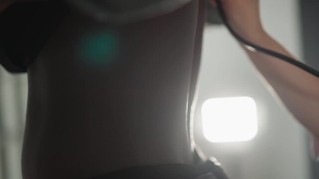 Stethoscope on mid back low light clinic scene, clinician adjusts tubing and earpiece while assessing breath sounds, soft lamp backlight creates silhouette, measured breathing and precise technique