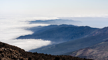 Obraz premium Stunning aerial view of a white sea of clouds rolling over pine forests and volcanic mountain ridges in Tenerife.