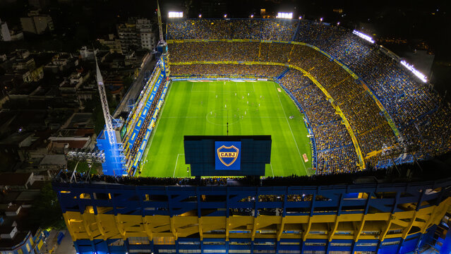 Buenos Aires, Argentina - November 23, 2025: Aerial night view of La Bombonera stadium during a match, featuring the Boca Juniors crest on the video board and the iconic blue and yellow architecture