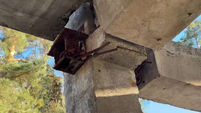 Concrete beams are being set up in a forest area. Workers are busy with installation tasks while the sun shines down among the trees. Tools and equipment are visible.