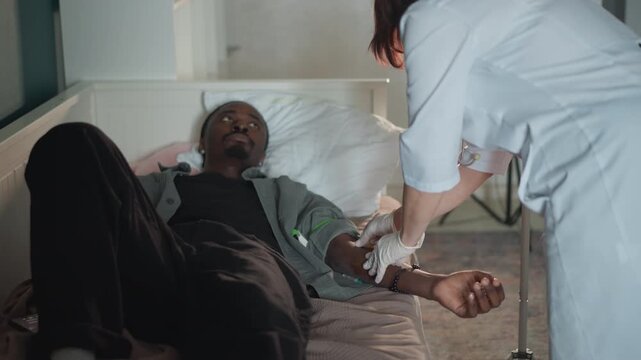 Black patient on bed receiving iv. Home nurse adjusts infusion tubing while monitoring vitals, caregiver applies bandage to catheter site, urgent clinical atmosphere with calm communication