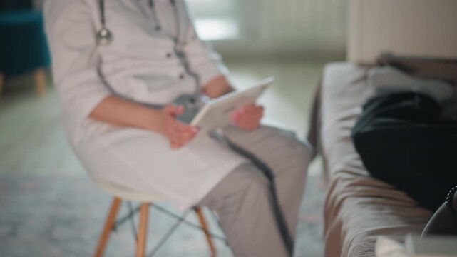 White female doctor conducting home consultation with patient on couch, stethoscope around neck, tablet notes visible, calm conversational assessment, attentive listening and professional reassurance,