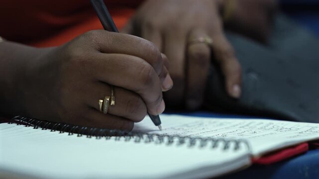 Close-up of woman's hands writing in spiral notebook