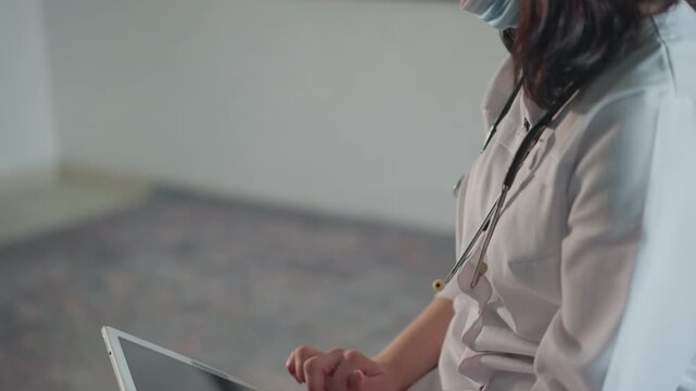 White nurse seated with tablet reflecting, mask lowered, reviewing appointment notes and scheduling in quiet clinical room tapping touchscreen, paperwork stacked, subdued colors, focused expression