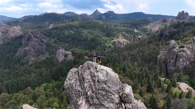 Awe-inspiring Aerial view of two rock climbers resting on the summit of a steep crag with a scenic forest background in Mineral del Chico, Hidalgo, Mexico, 4K horizontal dronie shot in a sunny day