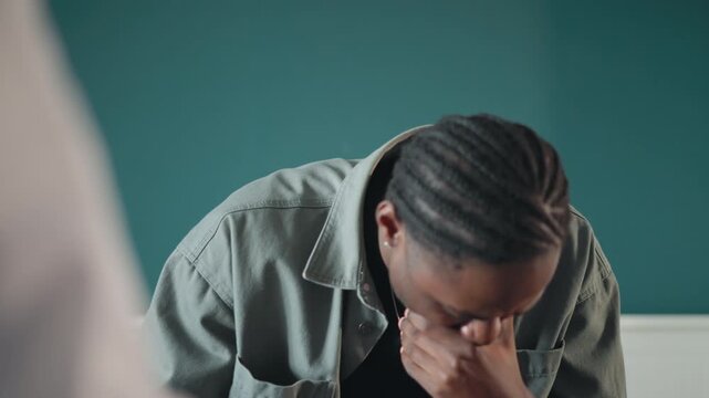 Black man during home consultation, hand over mouth, wiping tears with tissue, clinician blurred in foreground, receiving difficult diagnosis, solemn mood, compassionate atmosphere