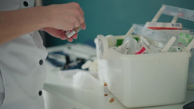 Nurse hands picking medication vials from kit, home visit setting with white uniform, careful selection of ampoules and syringes, organized plastic container, calm clinical lighting, attentive