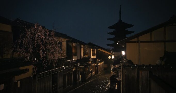 Empty, wet, ancient Japanese village with silhouetted temple tower - wide, dolly shot at night
