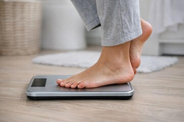 Fototapeta premium A person stands on a scale on a wooden floor, measuring their weight