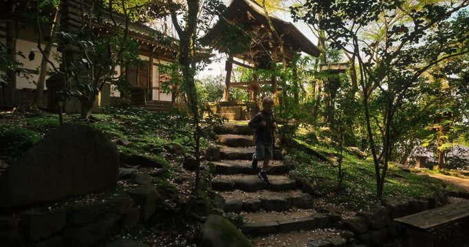 Little boy walking down stone steps of old Japanese village and foliage area - steady cam movement shot