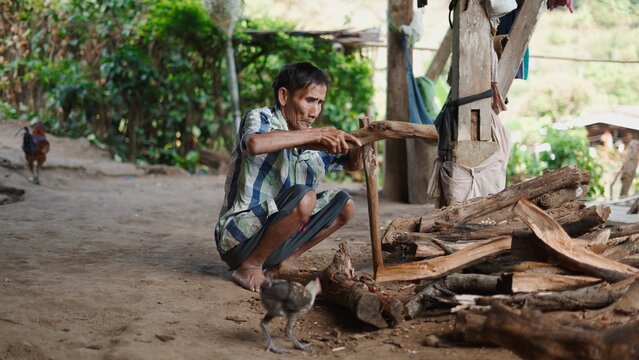 Old man squatting, splitting wood in a rural village, lifestyle and poverty concept