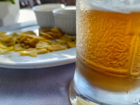 Vista parcial de un vaso con cerveza helada, de fondo. desenfocado, piqueo con acompa&ntilde;amiento de salsas