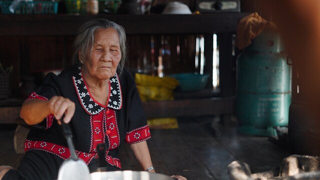 Elderly asian woman stirring food in traditional clothing at home
