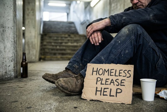 Desperate homeless man sitting on floor holding cardboard sign asking for help
