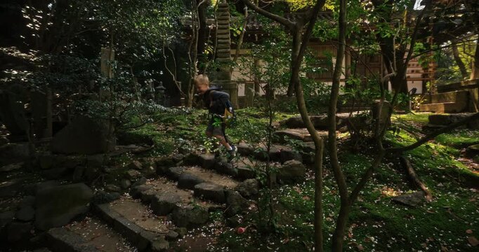 Cute little boy hopping down stone steps near old Japanese village building - steady cam shot