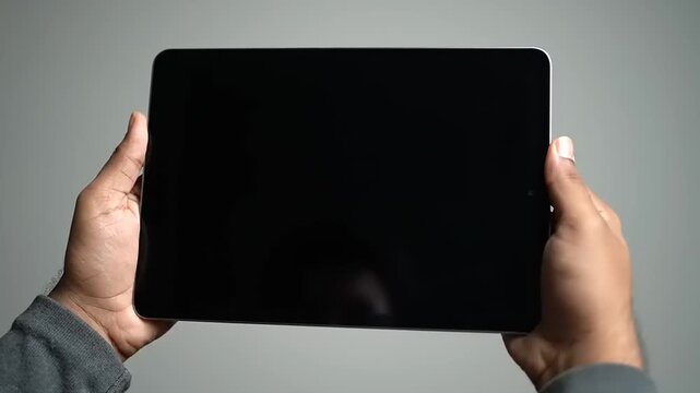 Person holding a tablet computer with a blank black screen, showcasing its display