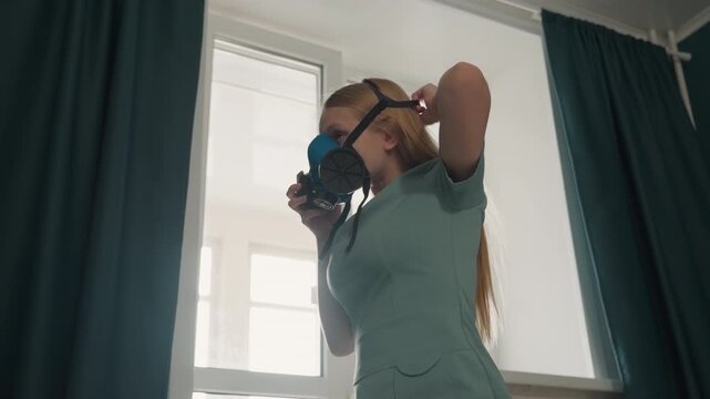 Caucasian homeowner examines respirator before house cleaning. Standing by window, checking straps and seal, adjusting mask, preparing to sanitize living spaces, daylight and dark curtains, practical