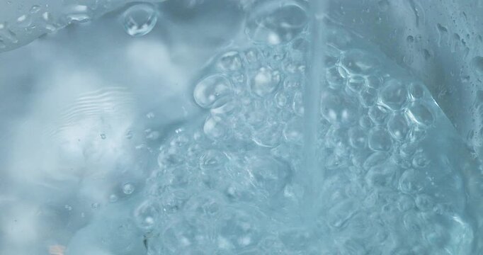 Acqua che scorre da un rubinetto in un contenitore di vetro formando bolle d'aria