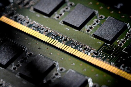 Computer RAM (Random Access Memory) memory module. Details of the gold contacts that fit into the motherboard and black flash memory chips soldered onto the green printed circuit board (PCB).