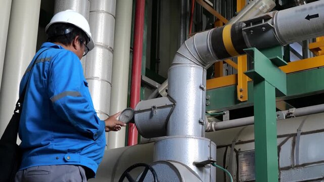 Industrial engineer monitoring process temperature through a mechanical thermometer gauge mounted on a pipeline represents process control, preventive maintenance, and efficient plant operation manage
