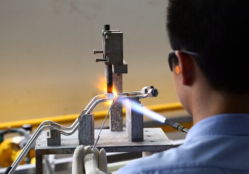 Shanghai, China - June 2022: A professional welder using a blowtorch to perform precision brazing on metal pipelines in a modern factory workshop, focusing on manufacturing craftsmanship.