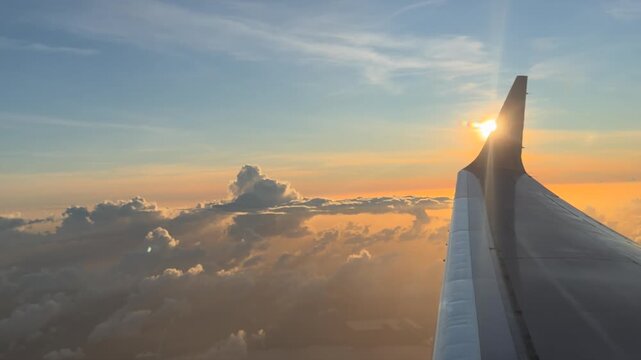 airplane wing flying through clouds at sunset with sun flare|